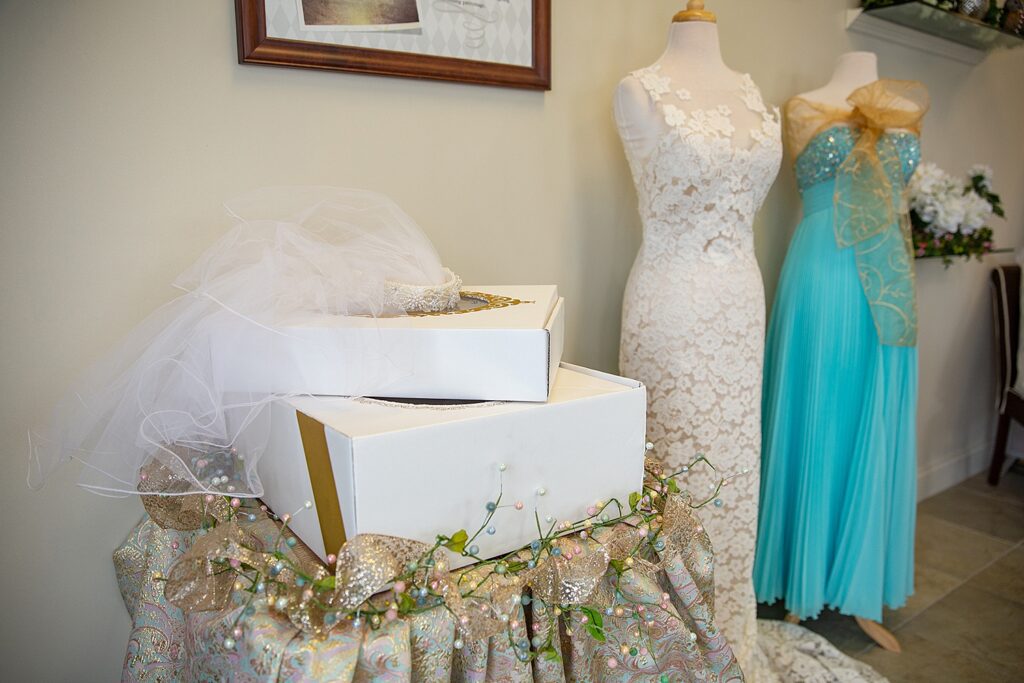 Two elegant mannequins display a white lace wedding dress and a turquoise gown with gold accents