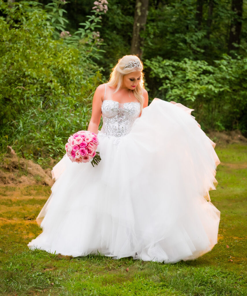 A bride in a flowing white gown adorned with intricate beadwork stands on a grassy path
