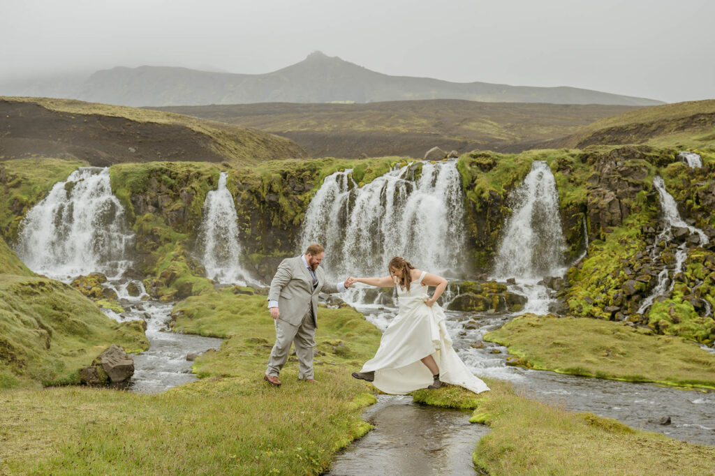 A couple in wedding attire walks hand in hand along a deserted black sand beach