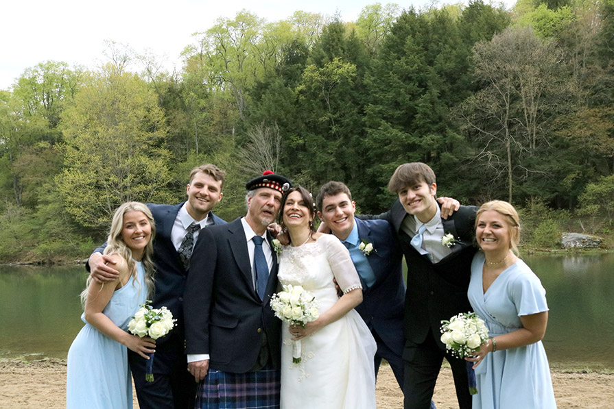 A joyful group poses by a lake, with lush green trees in the background