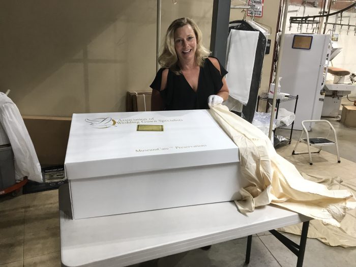 A woman stands smiling next to a large white box labeled "MuseumCare™ Preservation" on a table